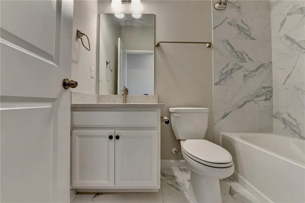 Bathroom with marble finish floor, tub / shower combination, vanity, and toilet