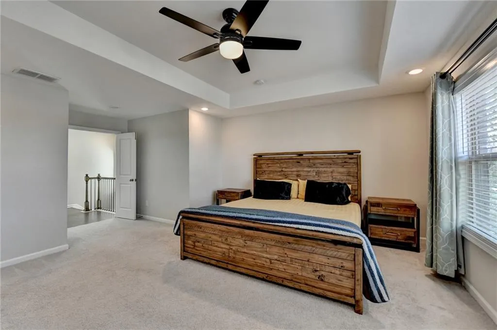 Bedroom with carpet floors, a raised ceiling, visible vents, and baseboards