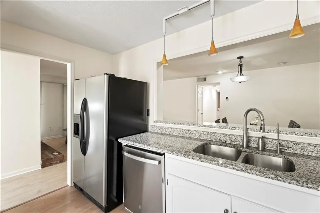 Kitchen with light wood-type flooring, dishwasher, light stone countertops, white cabinets, and decorative light fixtures Kitchen with light wood-type flooring, dishwasher, light stone countertops, white cabinets, and decorative light fixtures
