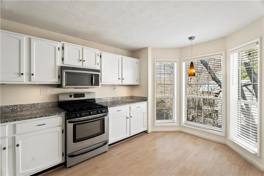 Kitchen with stainless steel appliances, white cabinets, decorative light fixtures, light wood-style flooring, and dark stone countertops Kitchen with stainless steel appliances, white cabinets, decorative light fixtures, light wood-style flooring, and dark stone countertops