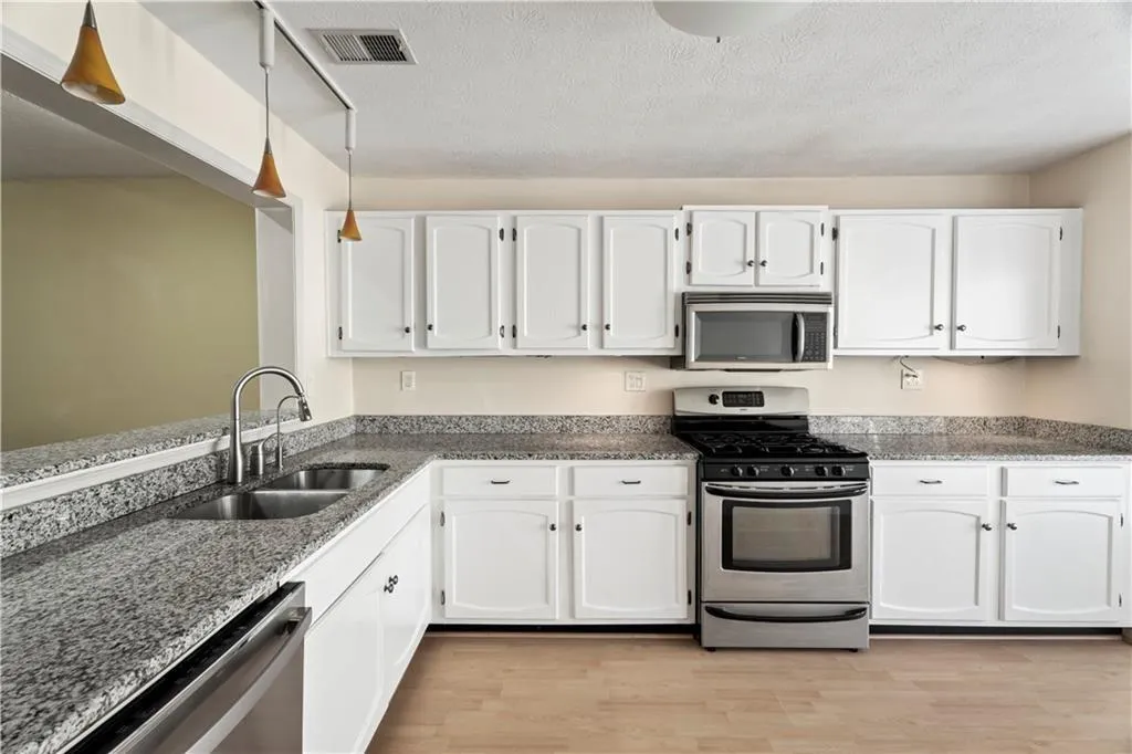 Kitchen with stainless steel appliances, white cabinets, dark stone countertops, a textured ceiling, and light wood-type flooring Kitchen with stainless steel appliances, white cabinets, dark stone countertops, a textured ceiling, and light wood-type flooring