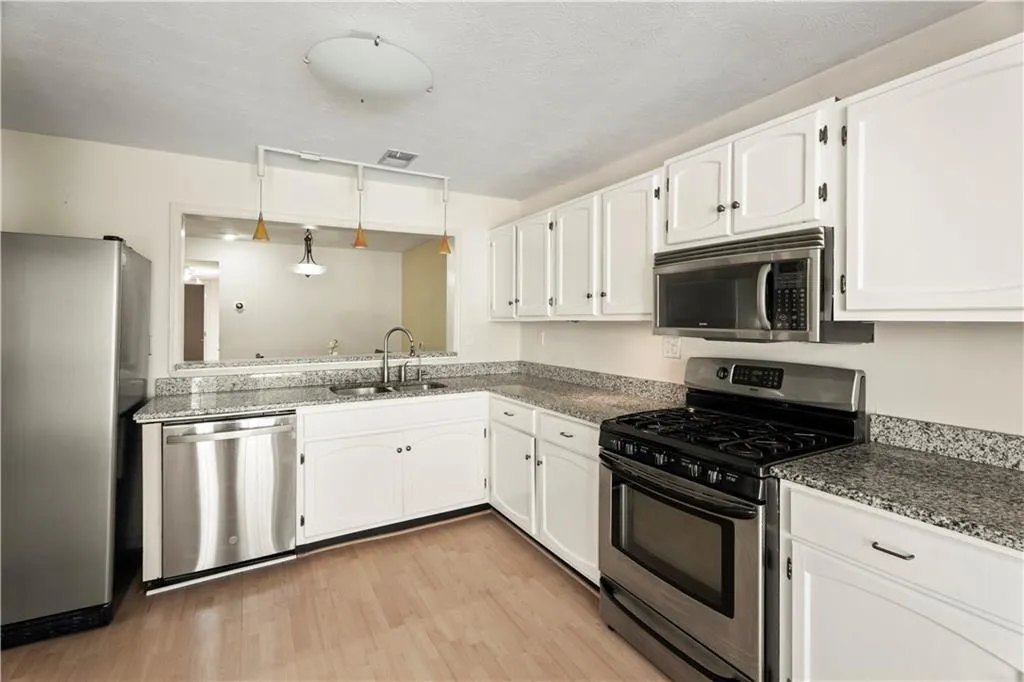 Kitchen featuring appliances with stainless steel finishes, light wood-style floors, white cabinetry, and dark stone counters Kitchen featuring appliances with stainless steel finishes, light wood-style floors, white cabinetry, and dark stone counters