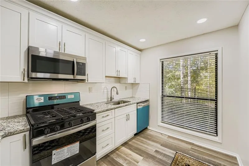 Kitchen featuring appliances with stainless steel finishes, white cabinets, decorative backsplash, light wood finished floors, and light stone countertops