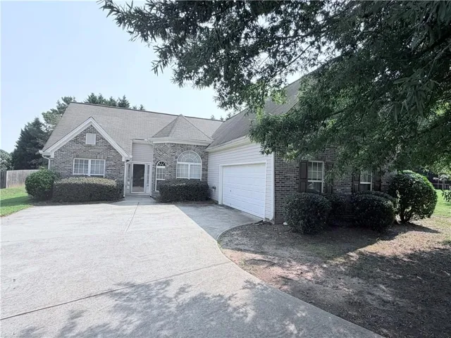 Traditional brick home featuring a prominent two-car garage with a white door, a concrete driveway, and mature landscaping