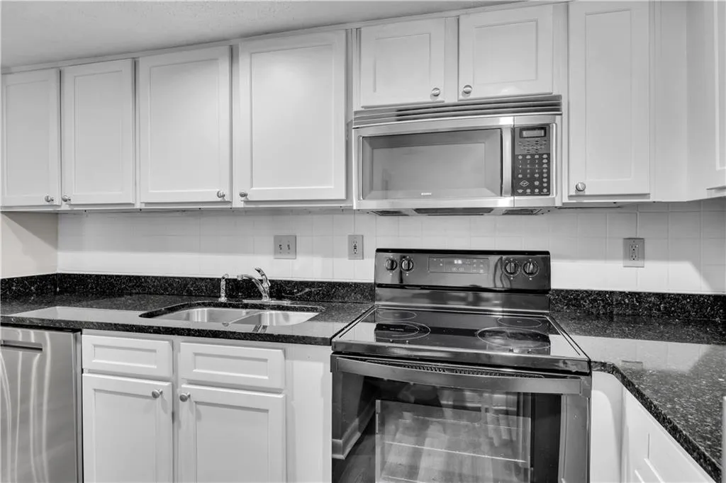 Kitchen featuring stainless steel appliances, dark stone countertops, backsplash, and white cabinetry