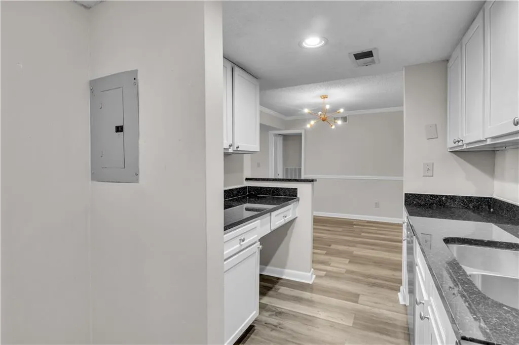 Kitchen with white cabinets, light wood finished floors, dark stone countertops, a chandelier, and electric panel