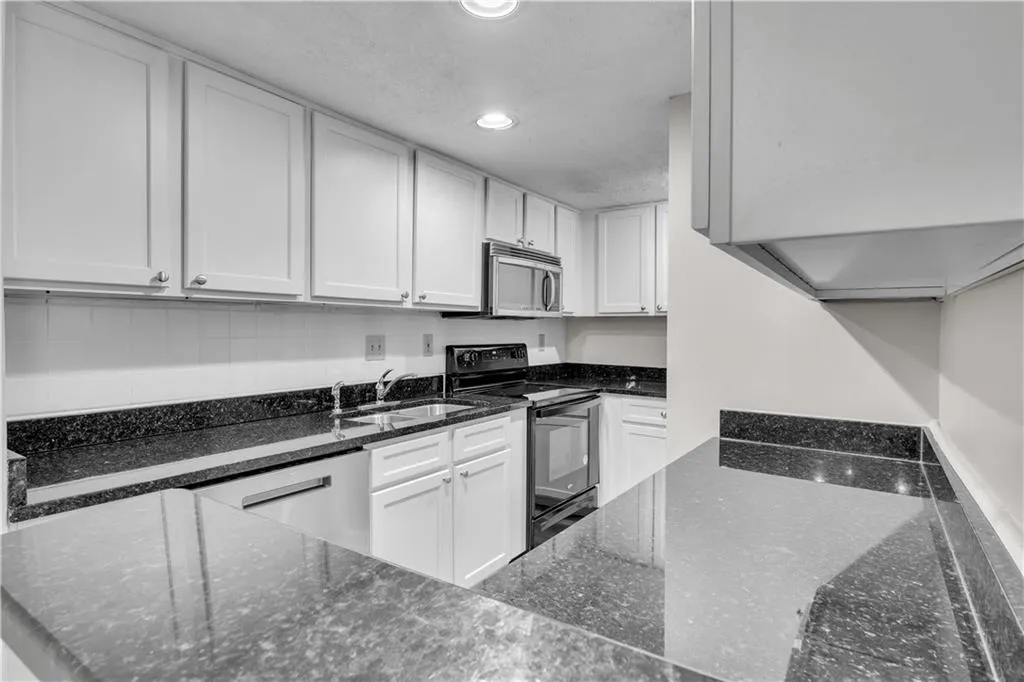 Kitchen with dark stone countertops, appliances with stainless steel finishes, white cabinets, recessed lighting, and a textured ceiling