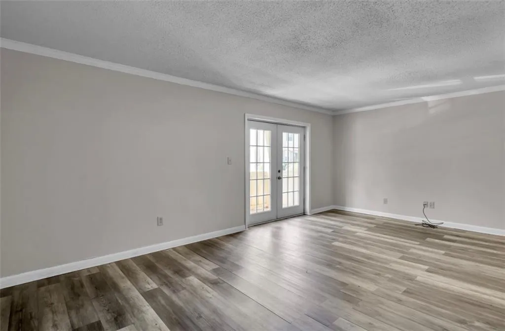 Empty room featuring french doors, ornamental molding, light wood-style floors, and a textured ceiling