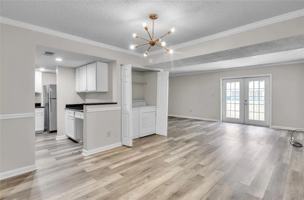 Unfurnished living room with crown molding, french doors, a textured ceiling, light wood-style floors, and a chandelier