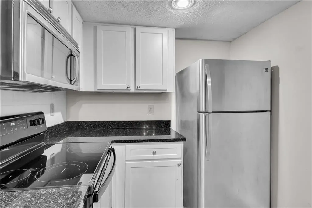 Kitchen featuring stainless steel appliances, white cabinets, a textured ceiling, and dark stone countertops