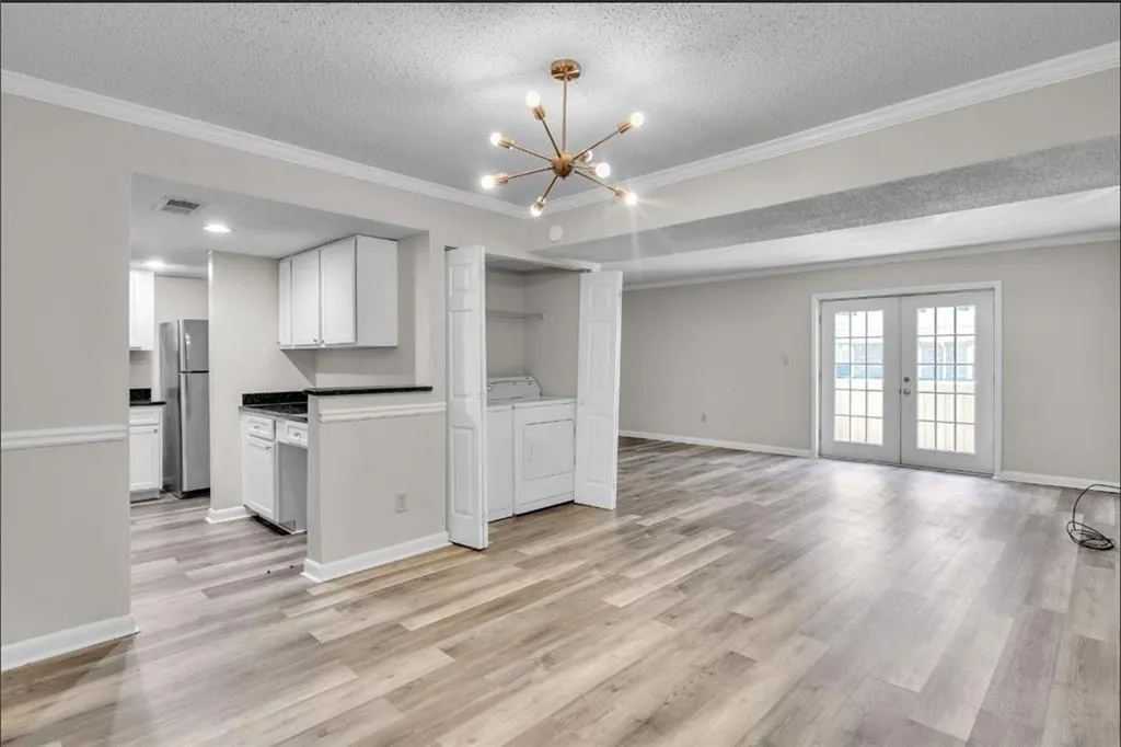 Unfurnished living room featuring ornamental molding, a textured ceiling, french doors, light wood-style floors, and a chandelier