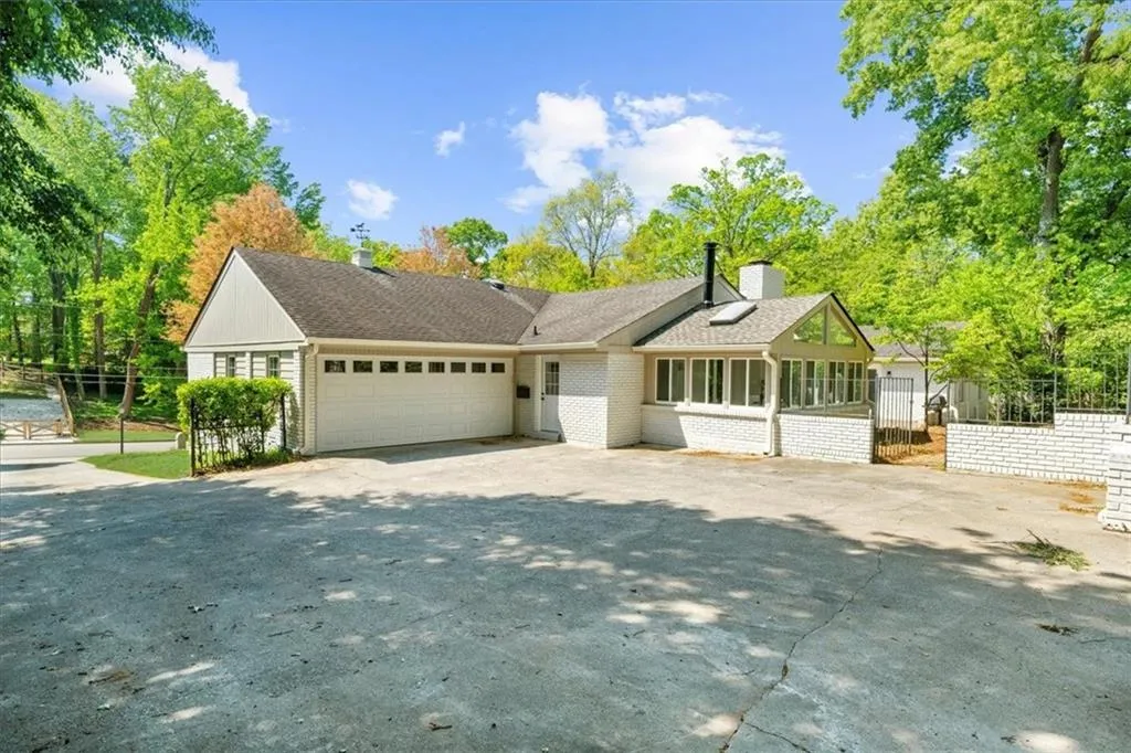 View of front of property featuring a chimney, driveway, an attached garage, fence, and a sunroom