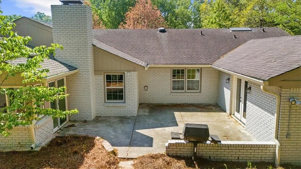 Back of property with a patio area, a shingled roof, a chimney, and brick siding