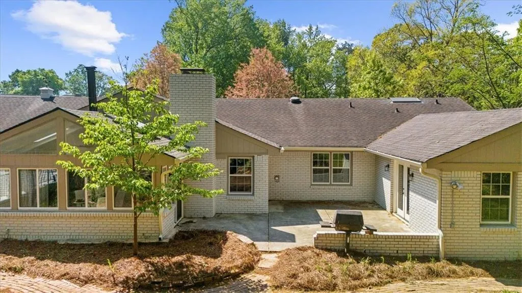 Back of house featuring a chimney, brick siding, a patio area, and a shingled roof