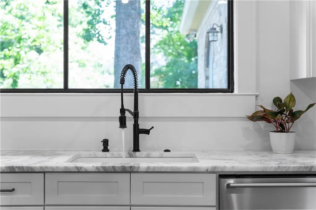 Detailed view of a sink, dishwasher, white cabinets, and light stone countertops
