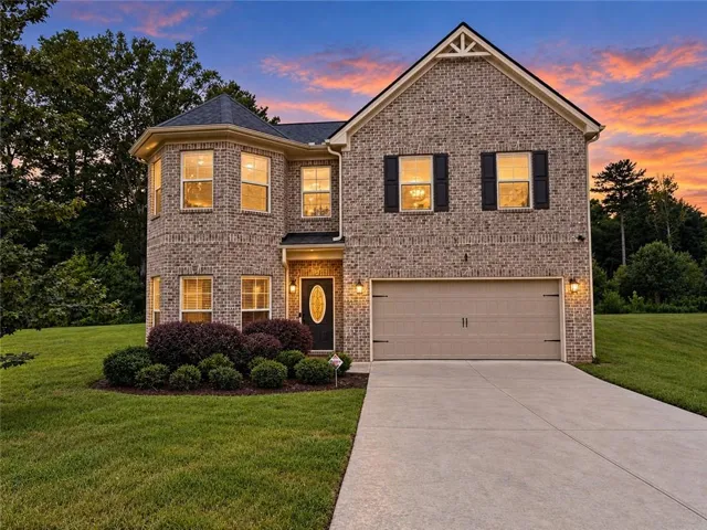 Brick exterior construction with a turret-style architectural element, an attached garage, a paved driveway, and mature landscaping