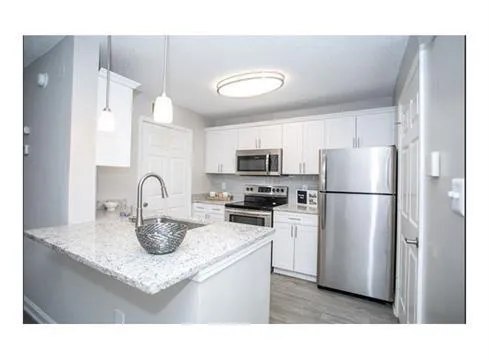 Kitchen featuring light hardwood / wood-style floors, pendant lighting, sink, white cabinetry, and appliances with stainless steel finishes