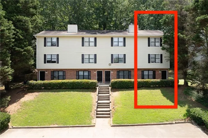 Two-story multi-unit structure featuring light-colored siding, dark shutters, a partial brick facade, and a tiered lawn with concrete stairs