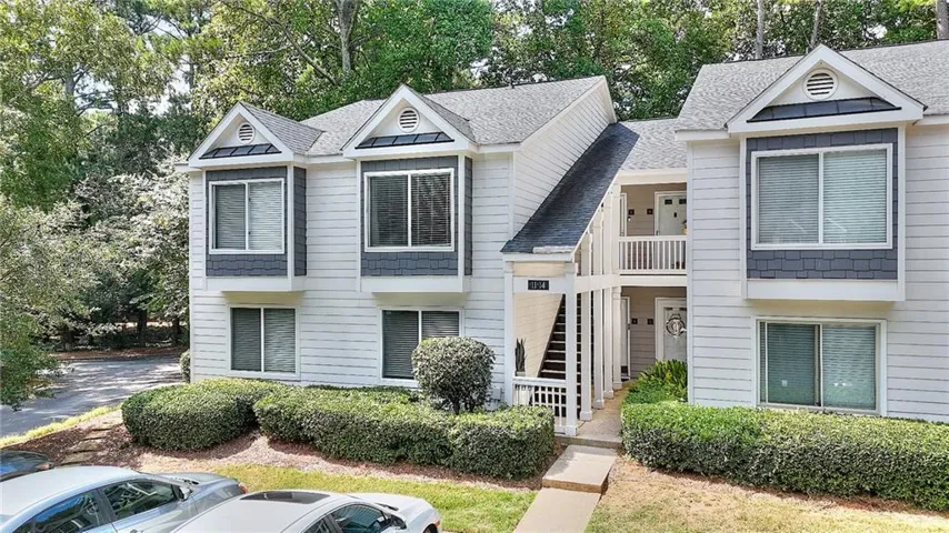 Multi-story building featuring light-colored siding, dark shingle roofing, and contrasting dark bay window accents
