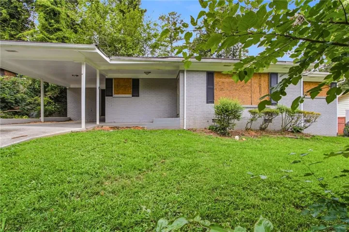 Exterior featuring a carport, brick facade, front lawn, and established shrubbery