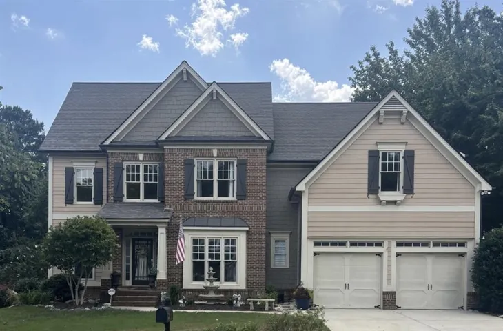 Brick and siding exterior with gabled roof lines, multiple windows with dark shutters, covered entry, and a two-car garage