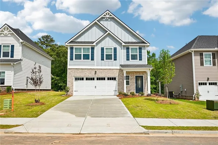 Two-story residence featuring light gray siding, brick veneer, a two-car garage, an asphalt shingle roof, and a concrete driveway