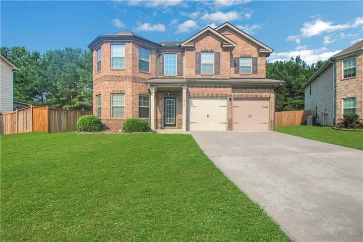Brick exterior featuring a two-car garage, mature landscaping, a concrete driveway, and a wooden privacy fence