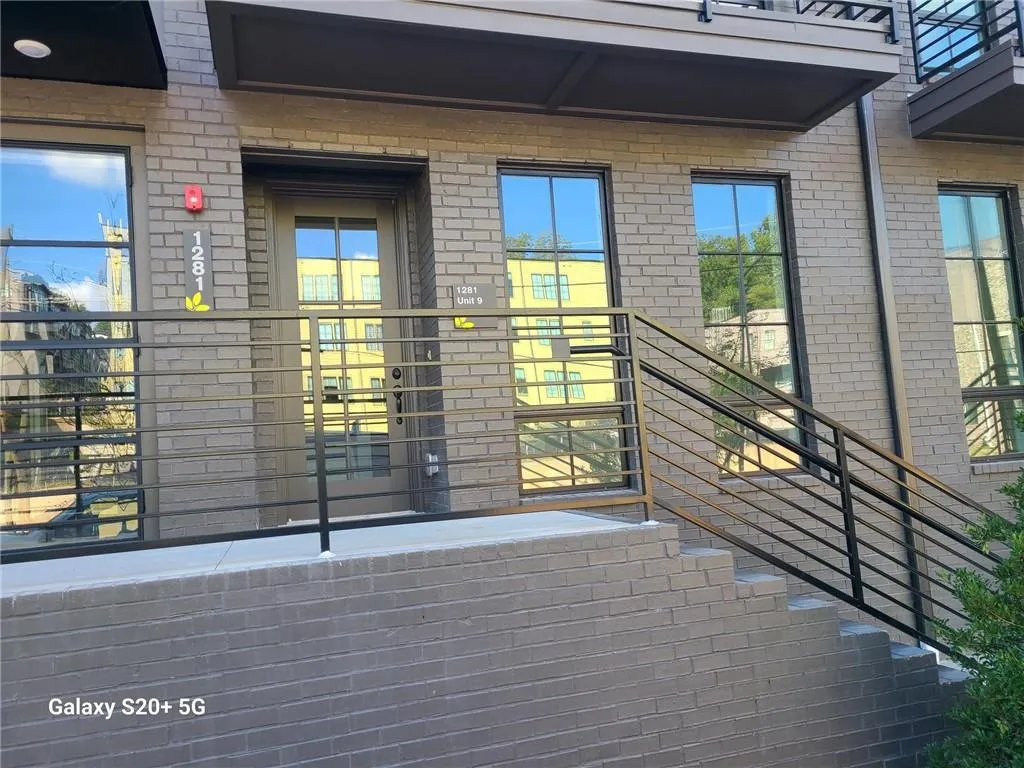 Brick exterior with dark-framed windows, a glass-paned entry door, and a metal railing system