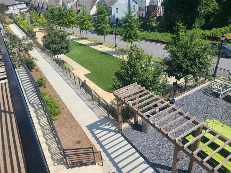 Paved walkway with metal fencing, manicured lawn, and mature trees