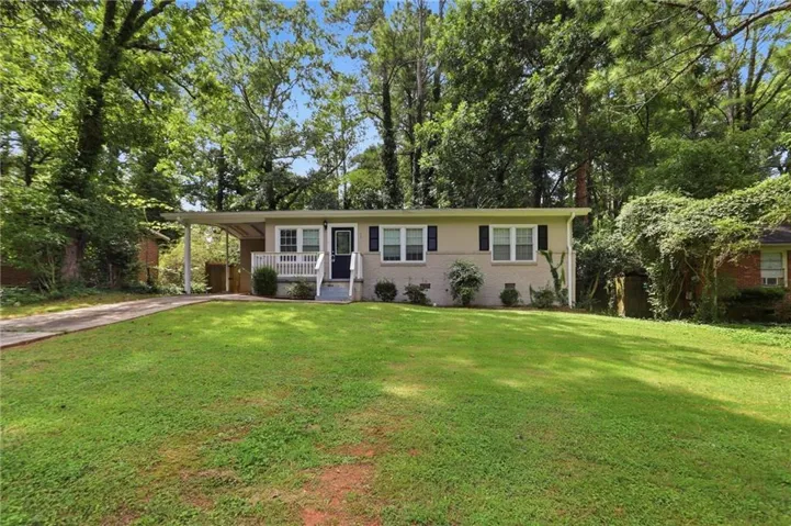 Single-story residence featuring a painted brick exterior, covered front porch with white railing, and a carport