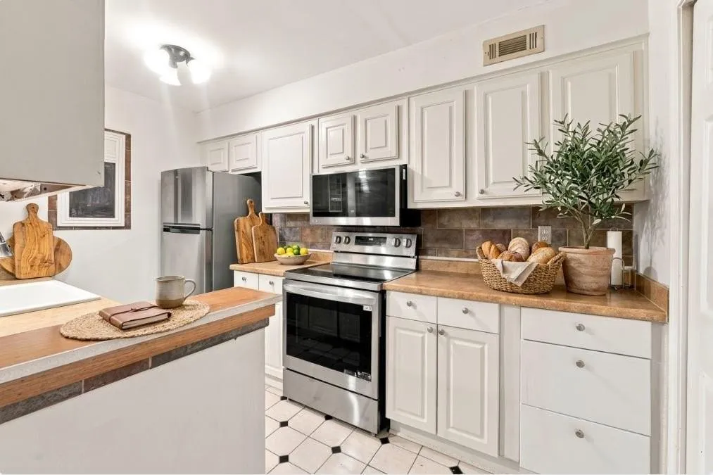 Kitchen featuring white cabinetry, stainless steel appliances, a tile backsplash, and stone-finish countertopsVirtually staged photo