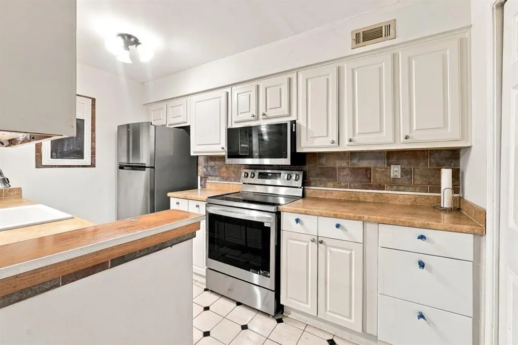 Kitchen with white cabinetry, stainless steel appliances, patterned floor tile, and a tile backsplash