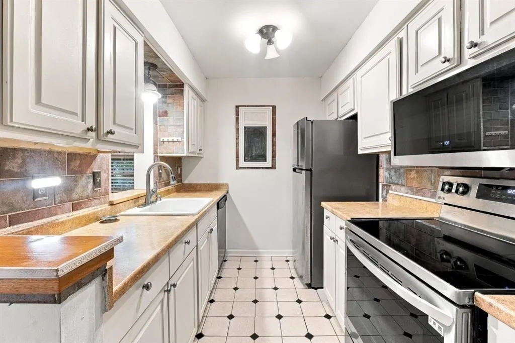 White cabinetry, stainless steel appliances, tile backsplash, laminate countertops, and patterned tile flooring