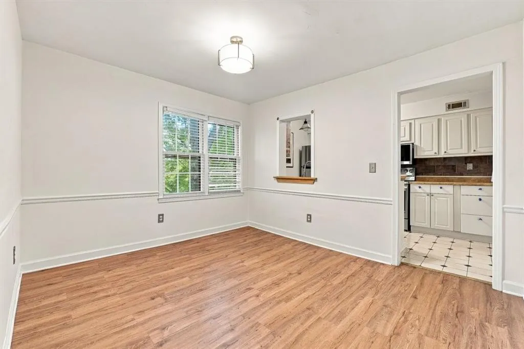 Wood-finish flooring, white walls with chair rail molding, window with blinds, pass-through opening, and an overhead light fixture