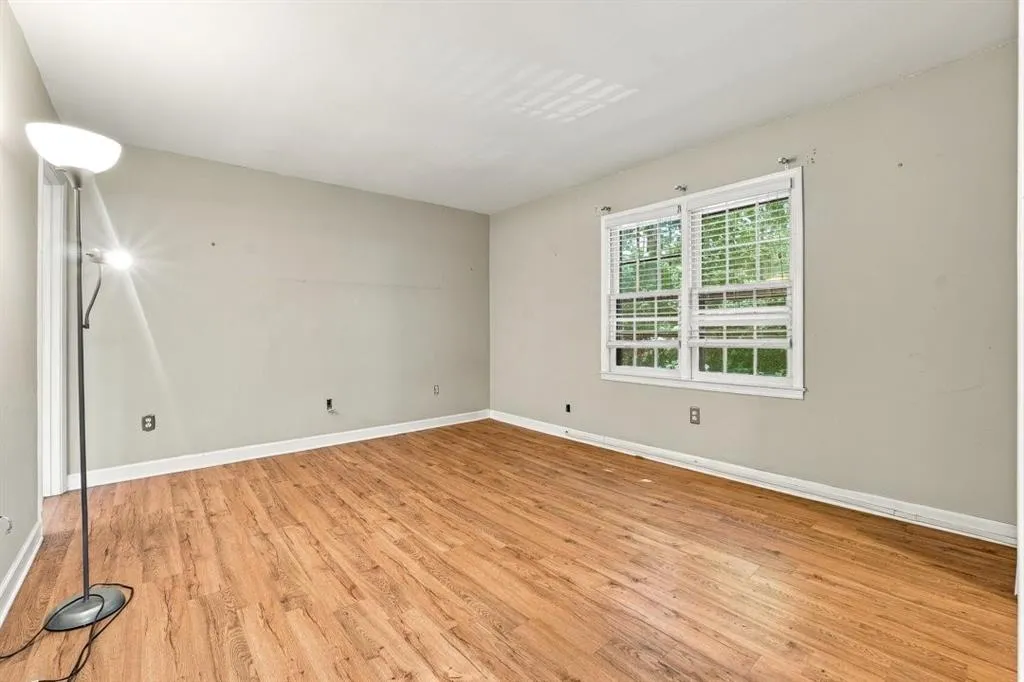 Wood-finish flooring with white trim, double windows with blinds, and light-colored walls