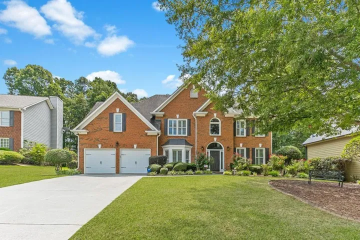 Brick facade with contrasting dark shutters, a two-car garage, a concrete driveway, and established landscaping