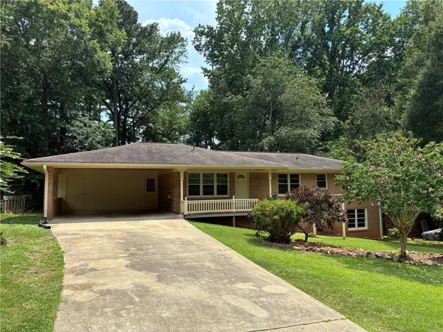 4 Sided Brick Exterior featuring a covered front porch with white railing, an attached carport, and a front yard with mature landscaping