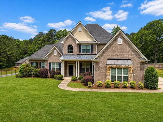 Brick exterior with stone accents, a gabled roofline, mature landscaping, an arched window, and a columned entry