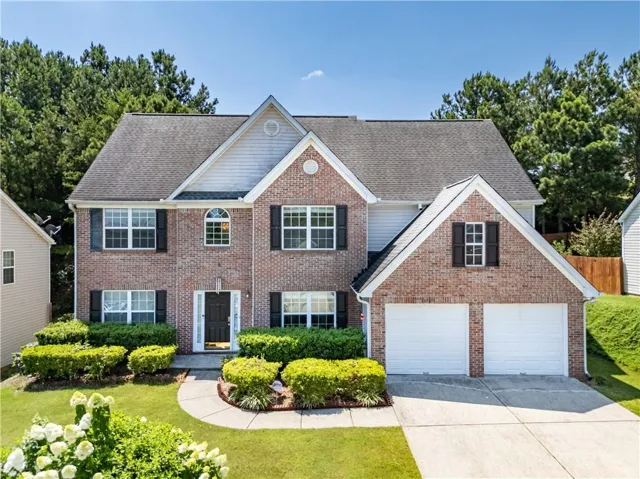 Colonial inspired home with a front yard, concrete driveway, roof with shingles, brick siding, and a garage