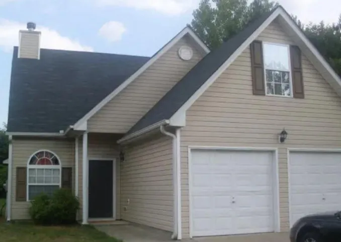 Two-car garage with panel doors, beige siding exterior, dark shingle roof, and a prominent chimney