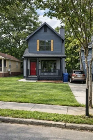 Gable-roof property featuring dark blue siding with a red front door, wood-finish window shutters, and a covered porch
