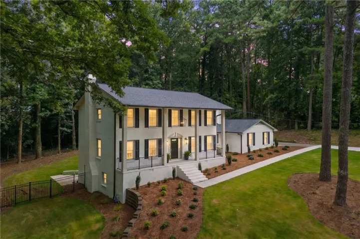 Two-story residence featuring white painted brick, black shutters, a dark gray roof, and a separate single-story structure