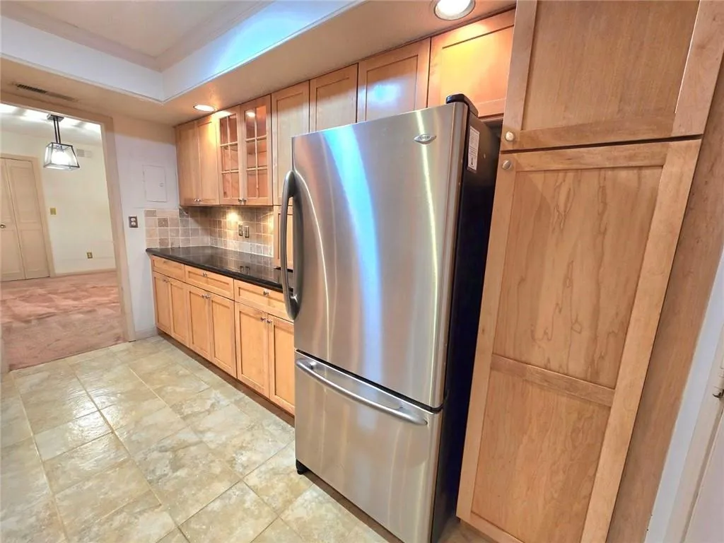 Kitchen featuring freestanding refrigerator, decorative backsplash, glass insert cabinets, light brown cabinetry, and ornamental molding