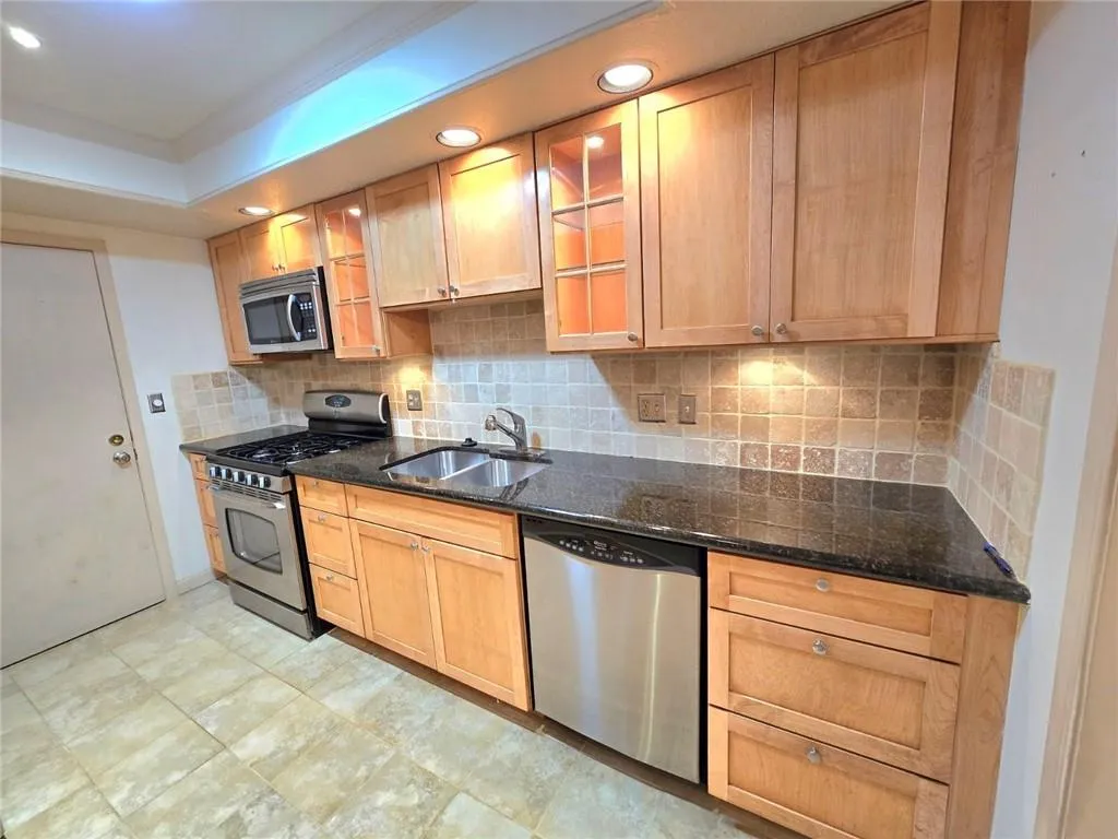 Kitchen featuring glass insert cabinets, appliances with stainless steel finishes, dark stone countertops, backsplash, and recessed lighting