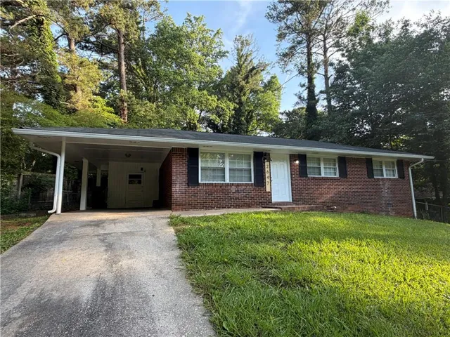 Brick exterior with a covered carport, concrete driveway, and front door with vertical numbering