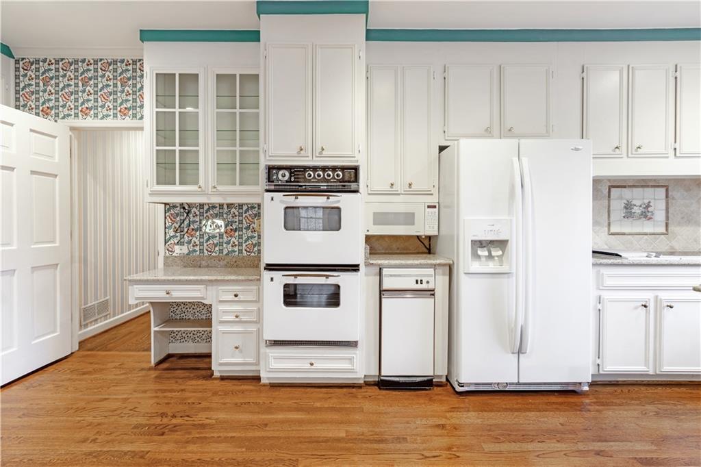 Kitchen with white cabinets, white appliances, backsplash, and hardwood flooring