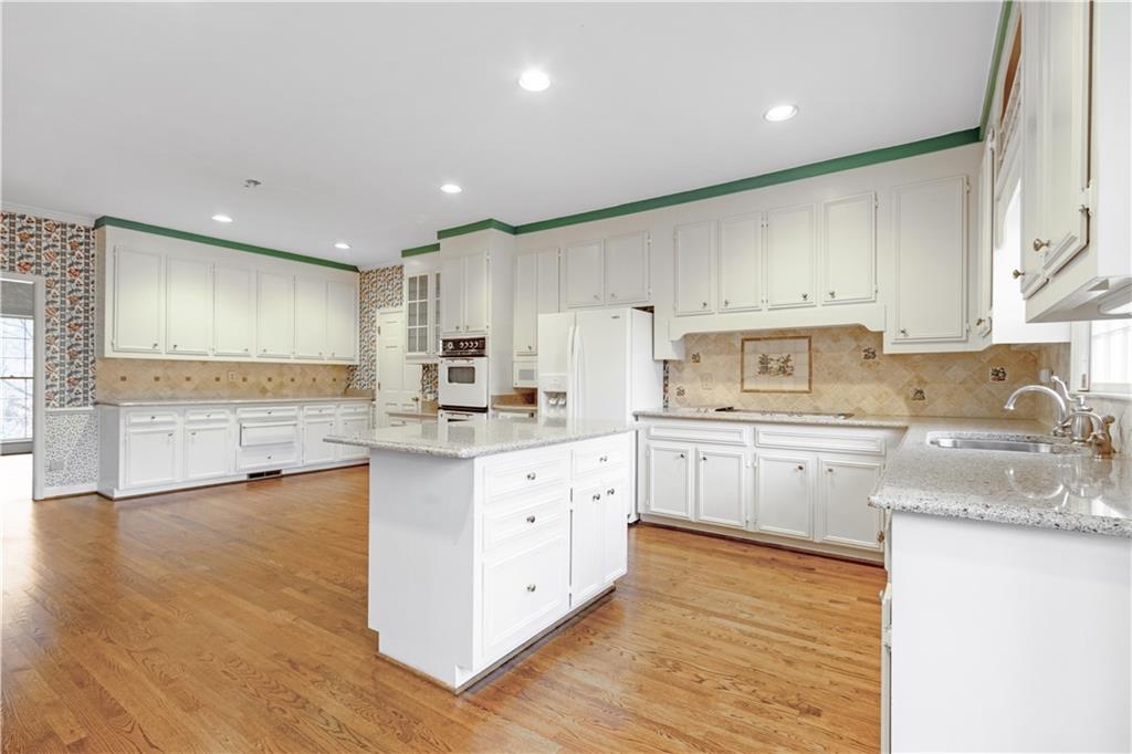 Kitchen with sink, hardwood floors, tasteful backsplash, white fridge with ice dispenser, and white cabinetry