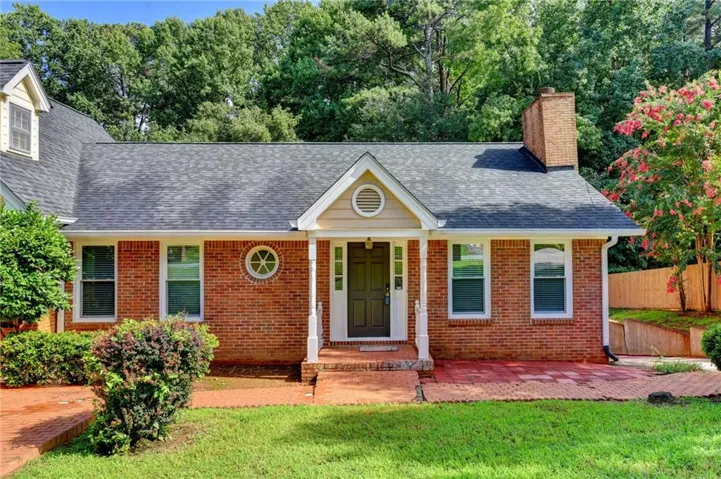 Brick facade residence featuring a covered front entry with white columns, a circular window accent, and a dark shingled roof