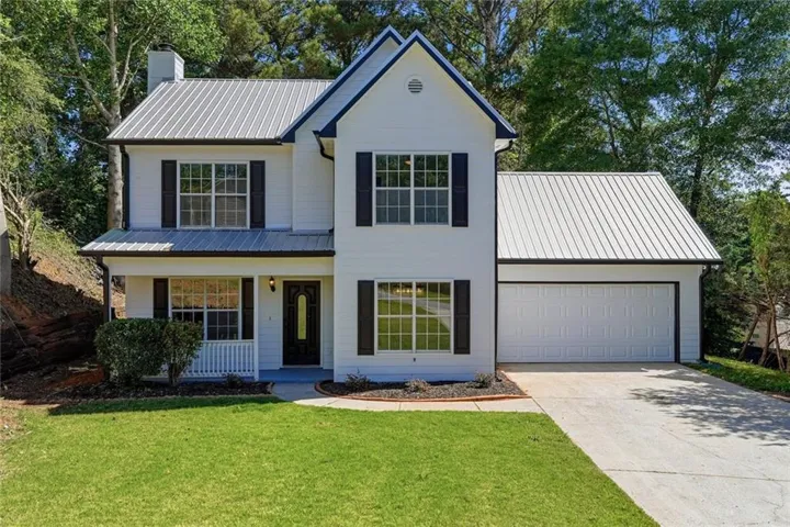 Contemporary exterior featuring white siding, a prominent metal roof, black window shutters, a covered porch, and an attached single-car garage with a concrete driveway