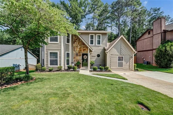 Siding exterior with stone accent, an attached garage, a mature tree, and a concrete driveway